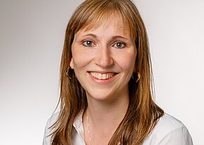 Christin Beyermann Porträt einer lächelnden Frau mit langen, braunen Haaren, die einen weißen Hemdkragen trägt. Der Hintergrund ist hell und neutral. Ihr Gesichtsausdruck ist freundlich und einladend.