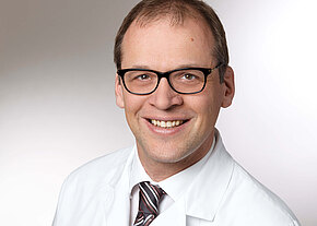 Univ.-Prof. Dr. med. Michael Vieth Porträt eines lächelnden Mannes mit Brille in weißem Arztkittel und gestreifter Krawatte vor neutralem Hintergrund.