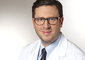 Prof. Dr. med. Stefan Förster Porträtfoto einer erwachsenen Person mit Brille in weißem Arztkittel und Krawatte, lächelt leicht, Blick in die Kamera vor neutralem Hintergrund.